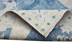 A vintage Persian Kerman rug featuring a blue and cream floral pattern with a folded corner.