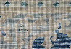 A close-up of a vintage Persian Kerman rug featuring intricate blue floral patterns on a beige base.