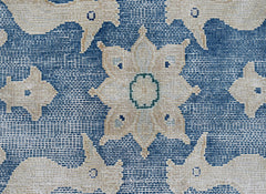 A close-up of a vintage Persian Kerman rug featuring a central floral medallion on a blue field.