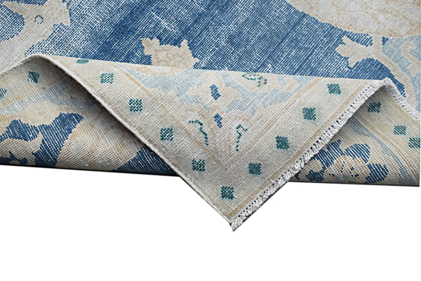 A vintage Persian Kerman rug featuring a blue and cream floral pattern with a folded corner.