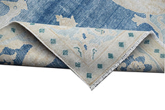 A vintage Persian Kerman rug featuring a blue and cream floral pattern with a folded corner.
