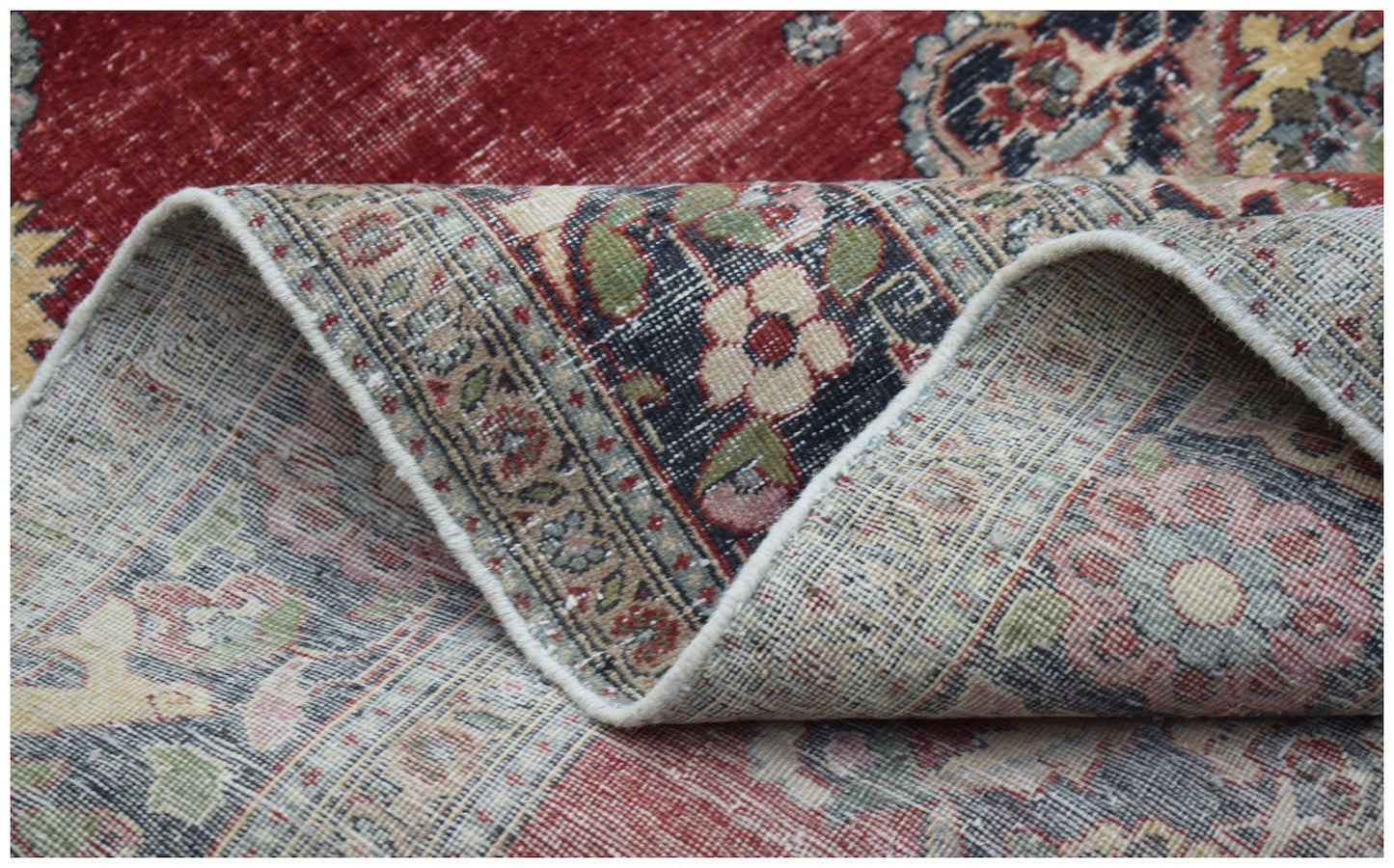 A folded vintage Persian Kerman rug featuring a red field and intricate floral medallion patterns.