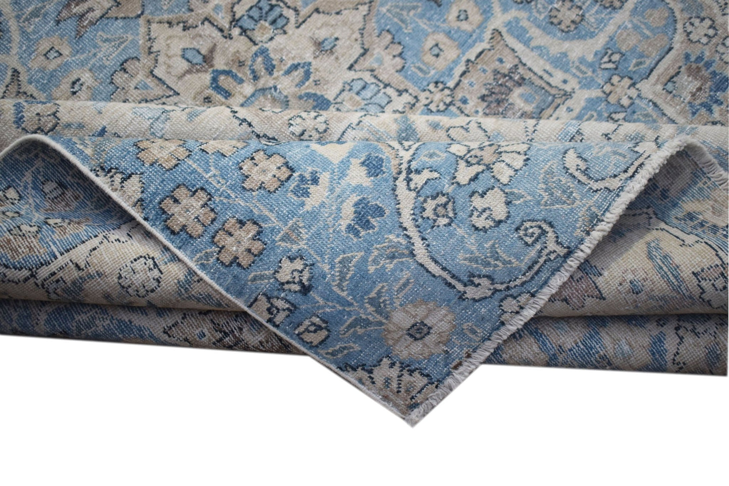A vintage Persian Kerman rug featuring a blue and beige floral pattern with a folded corner.
