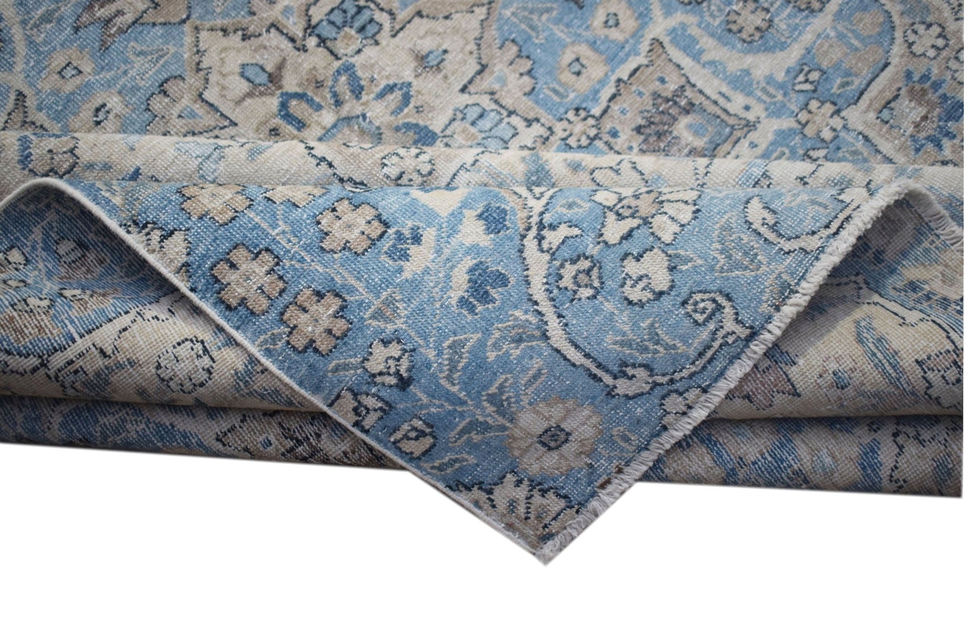 A vintage Persian Kerman rug featuring a blue and beige floral pattern with a folded corner.