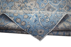 A vintage Persian Kerman rug featuring a blue and beige floral pattern with a folded corner.