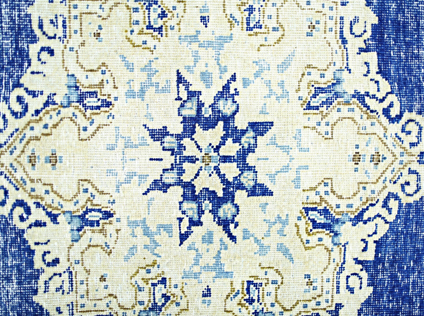 A vintage Persian Kerman rug featuring a central blue star medallion on a cream background.