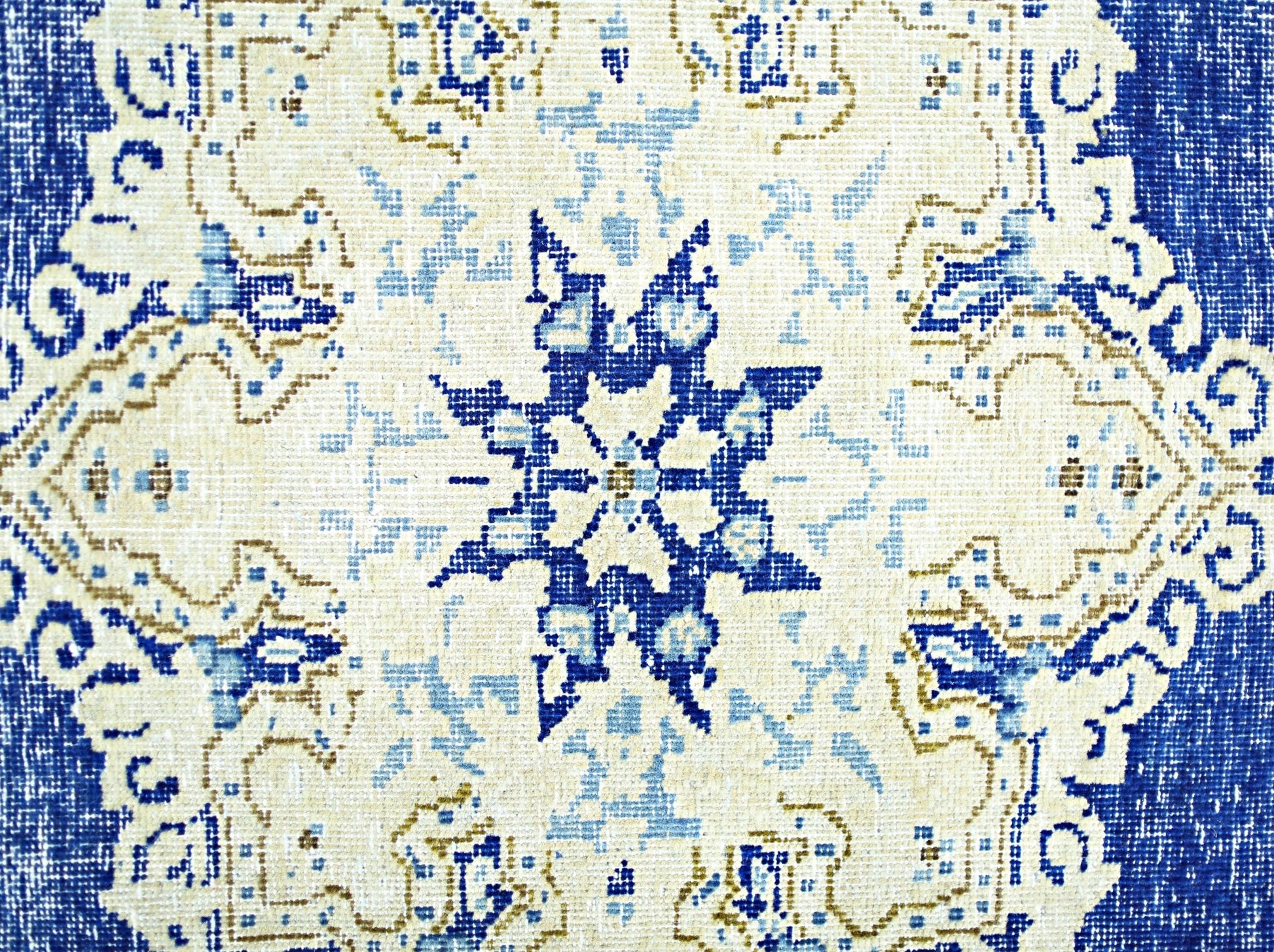 A vintage Persian Kerman rug featuring a central blue star medallion on a cream background.