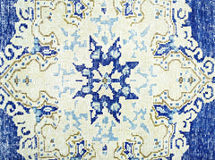 A vintage Persian Kerman rug featuring a central blue star medallion on a cream background.