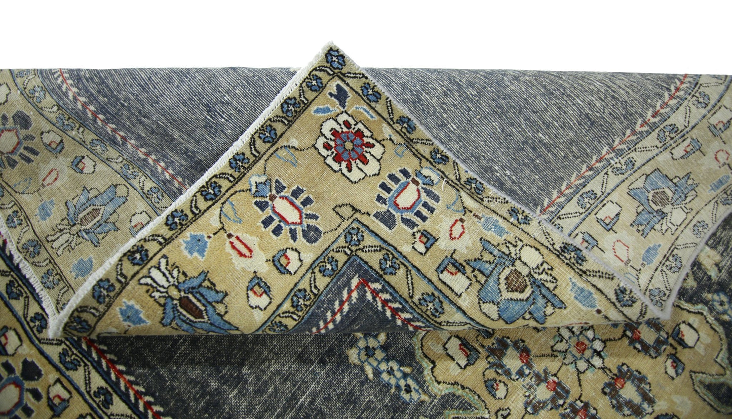 A vintage Persian Kerman rug with a folded corner revealing a blue and beige floral pattern.