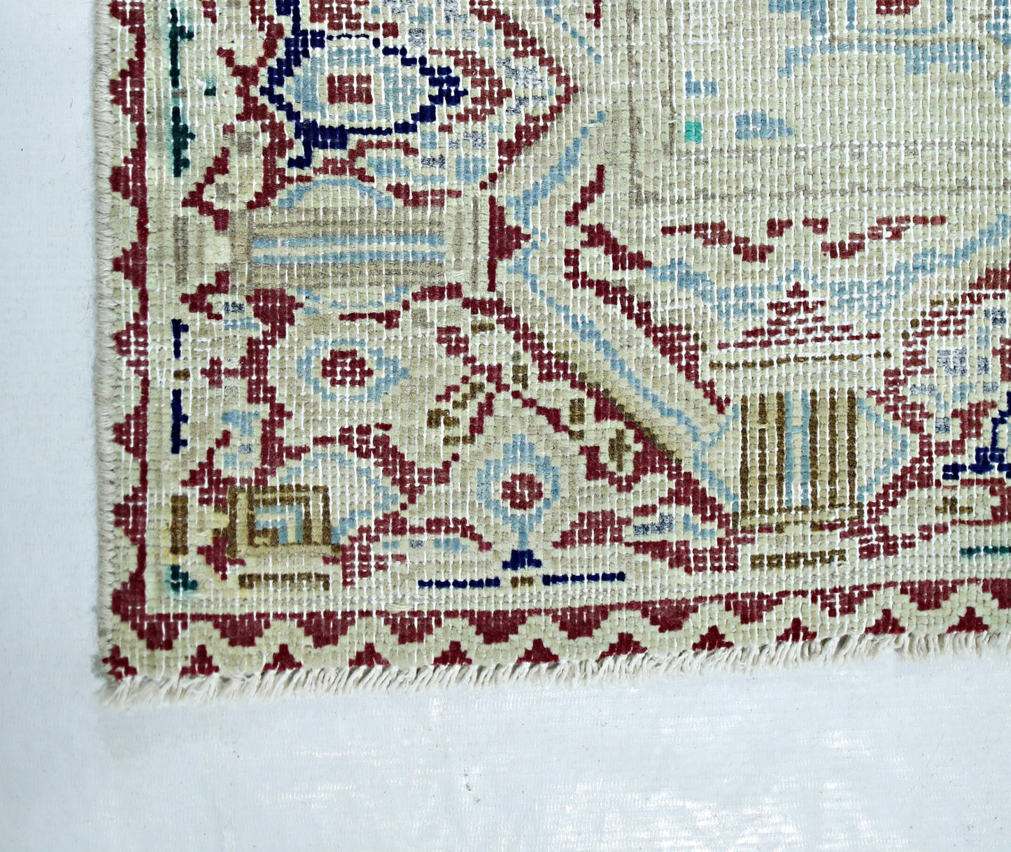A corner view of a vintage Persian Kerman rug featuring intricate floral patterns and a fringe.