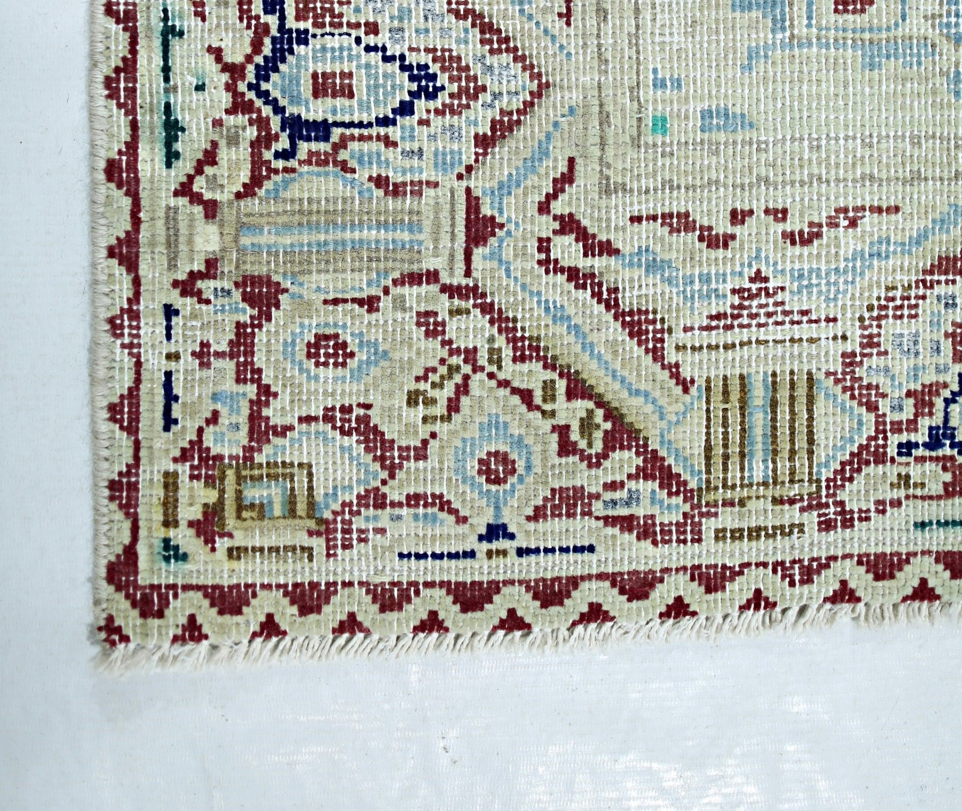 A corner view of a vintage Persian Kerman rug featuring intricate floral patterns and a fringe.
