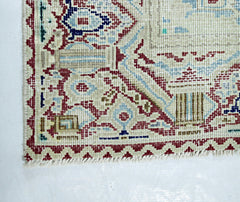 A corner view of a vintage Persian Kerman rug featuring intricate floral patterns and a fringe.
