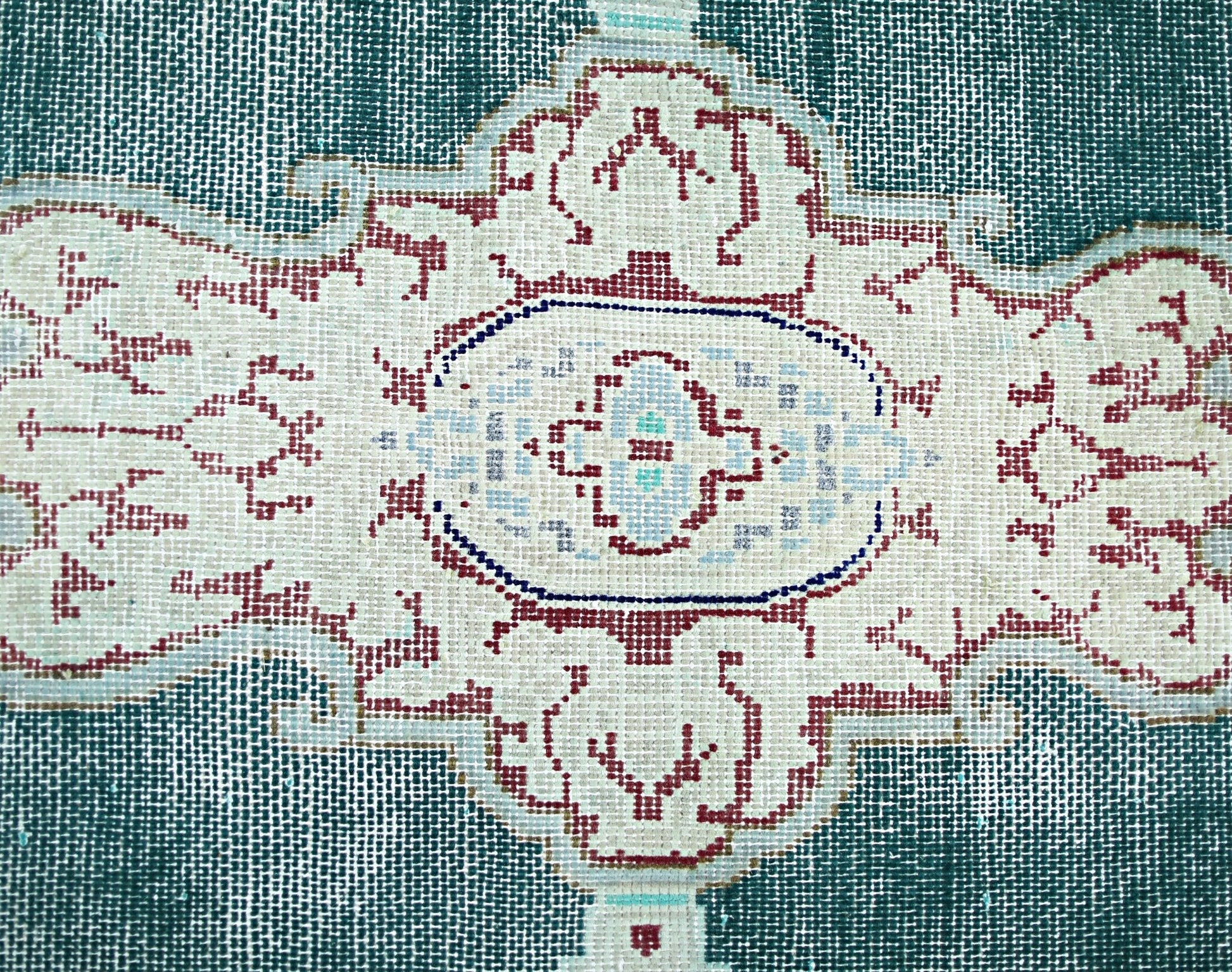 A close-up of a vintage Persian Kerman rug featuring an intricate floral medallion in teal and red.