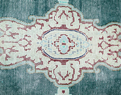 A close-up of a vintage Persian Kerman rug featuring an intricate floral medallion in teal and red.