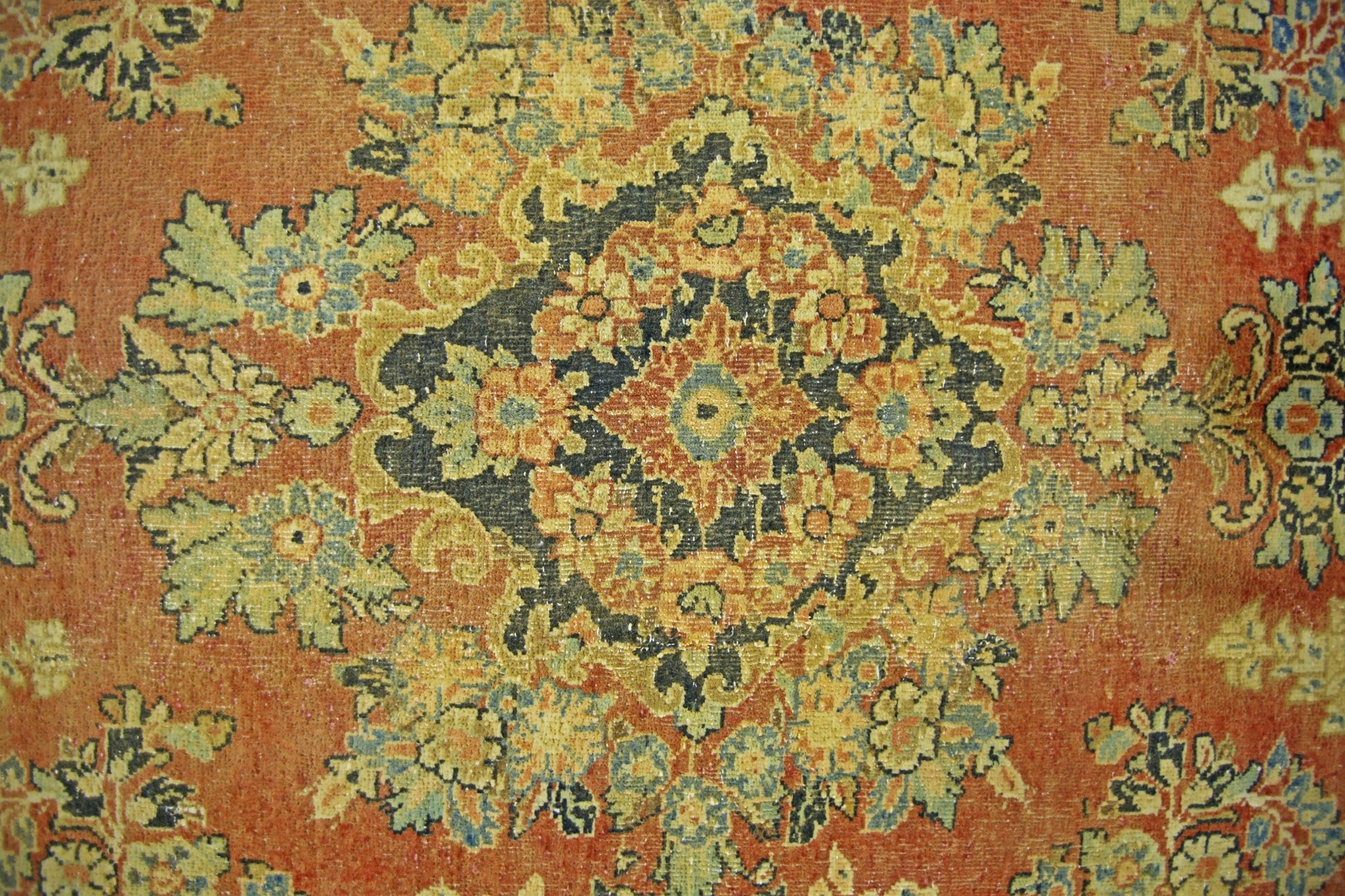 A vintage Persian Kerman rug featuring an intricate floral medallion on a warm orange background.