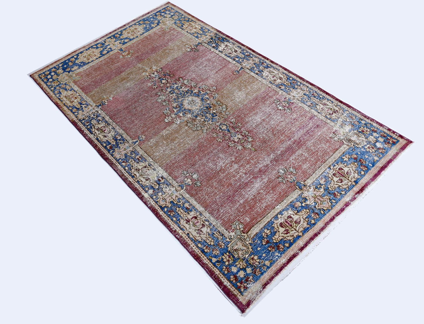 A vintage Persian Kerman rug featuring a central floral medallion on a faded red and tan field.