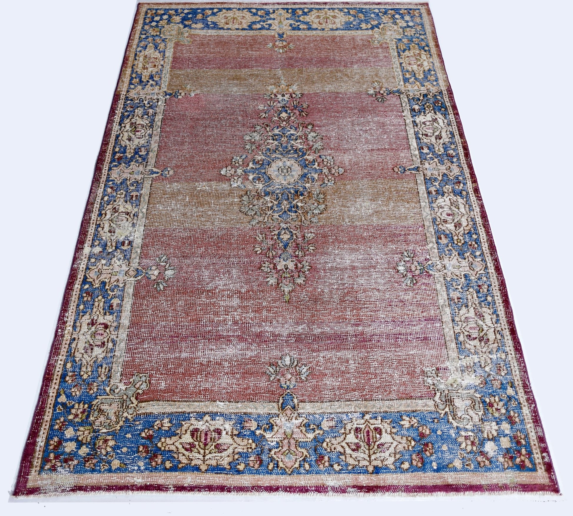 A vintage Persian Kerman rug featuring a central medallion and floral border in red and blue tones.
