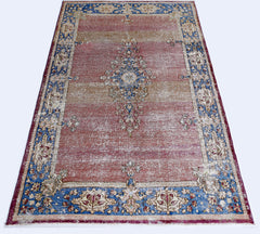 A vintage Persian Kerman rug featuring a central medallion and floral border in red and blue tones.