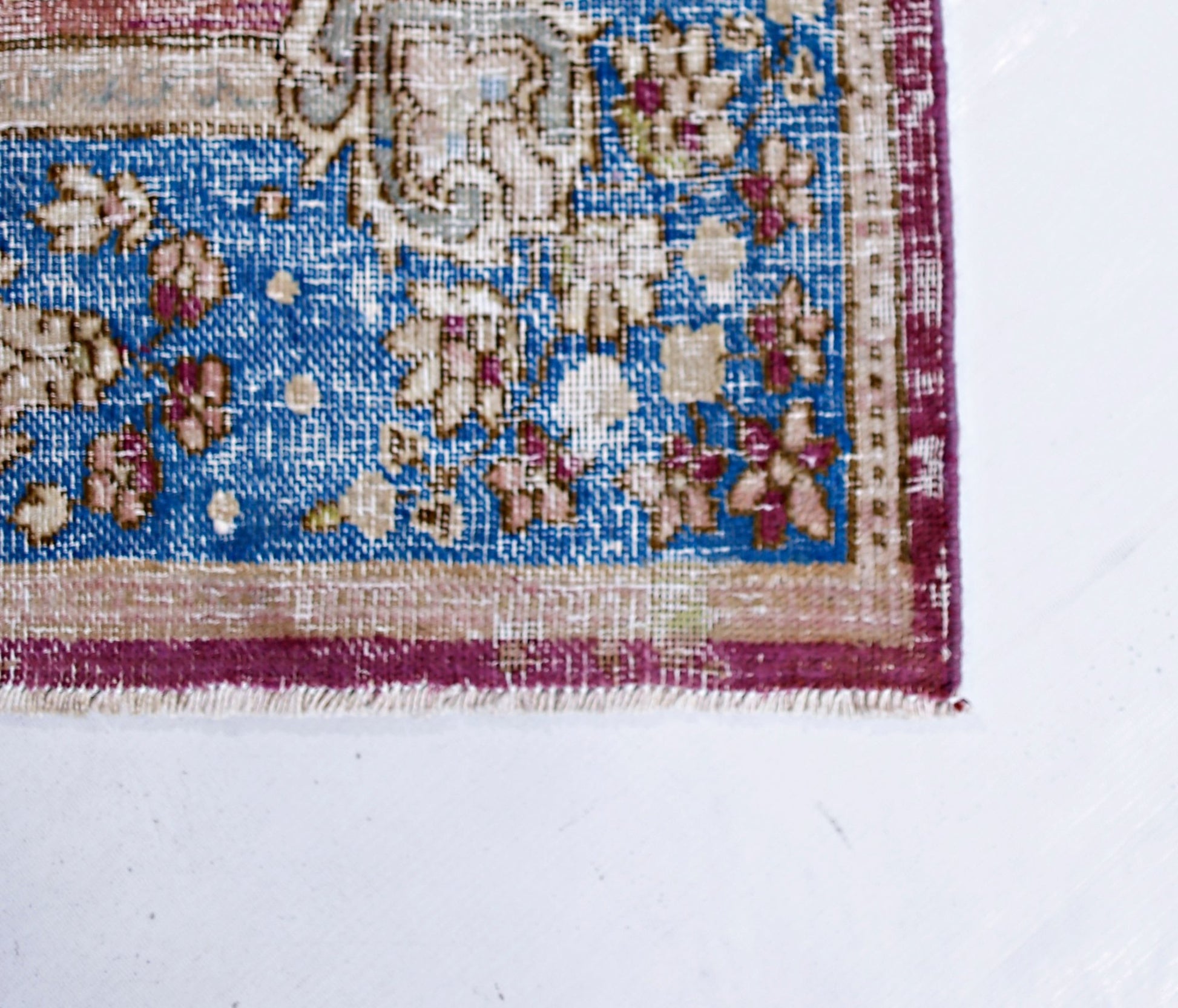 A corner view of a vintage Persian Kerman rug featuring a blue field with intricate floral patterns.