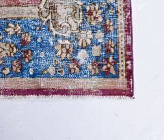 A corner view of a vintage Persian Kerman rug featuring a blue field with intricate floral patterns.