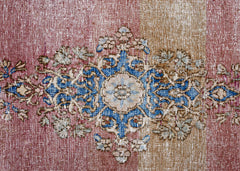 A vintage Persian Kerman rug featuring a central blue and cream floral medallion on a faded red and tan background.