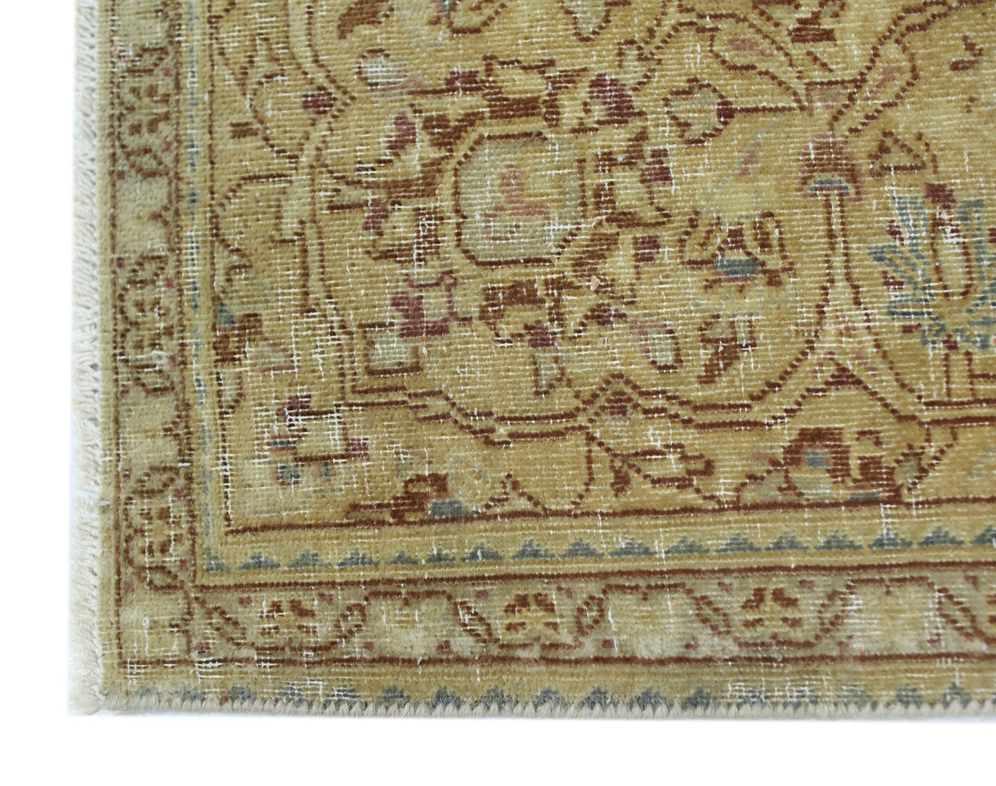 A corner view of a vintage Persian Kerman rug featuring a faded floral medallion and border.