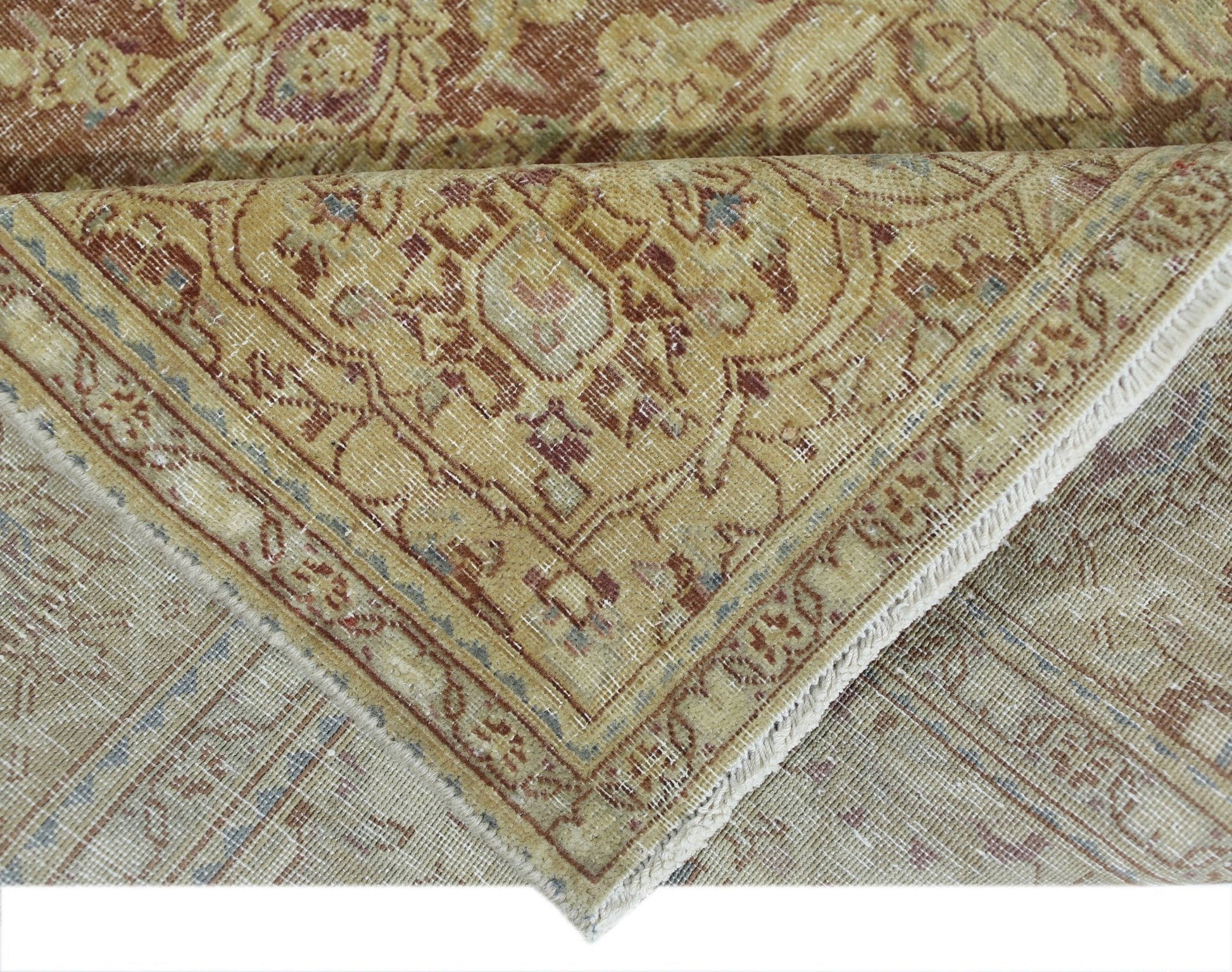 A corner of a vintage Persian Kerman rug showing a folded edge with intricate floral patterns.