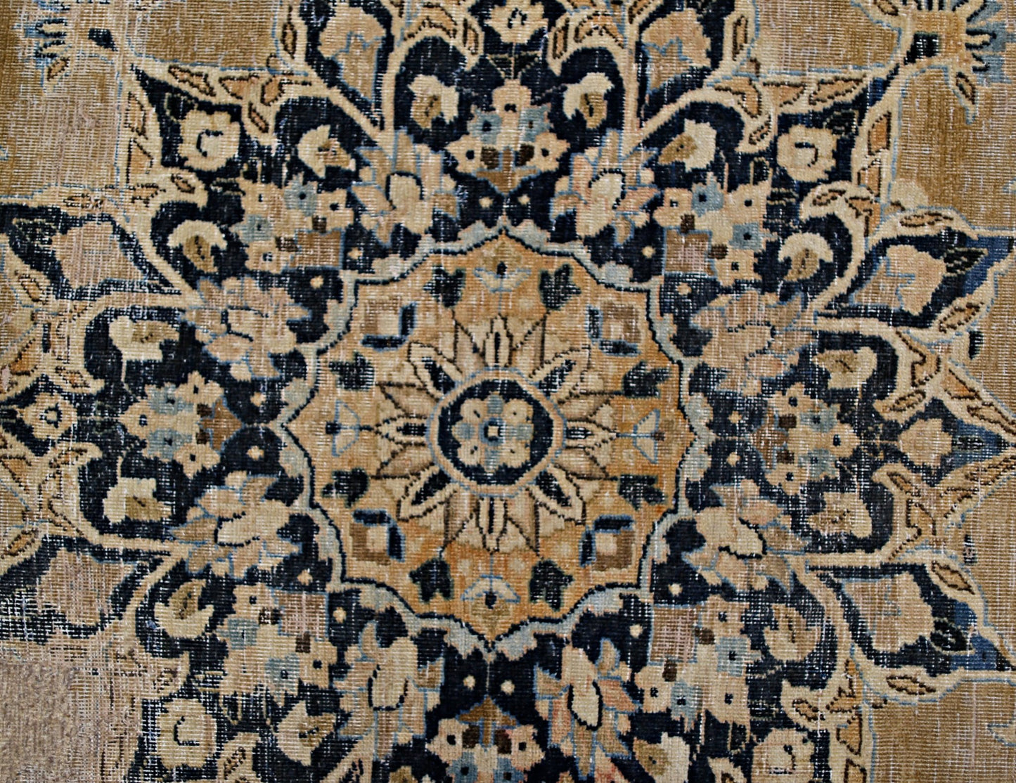 A vintage Persian Kerman rug featuring an intricate floral medallion in tan and navy blue.
