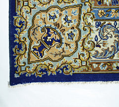 A corner view of a vintage Persian Kerman rug featuring intricate floral patterns in blue and tan.