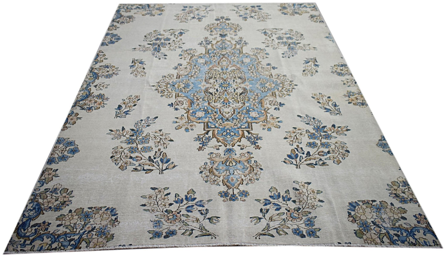A vintage Persian Kerman rug featuring a central blue medallion and intricate floral motifs.