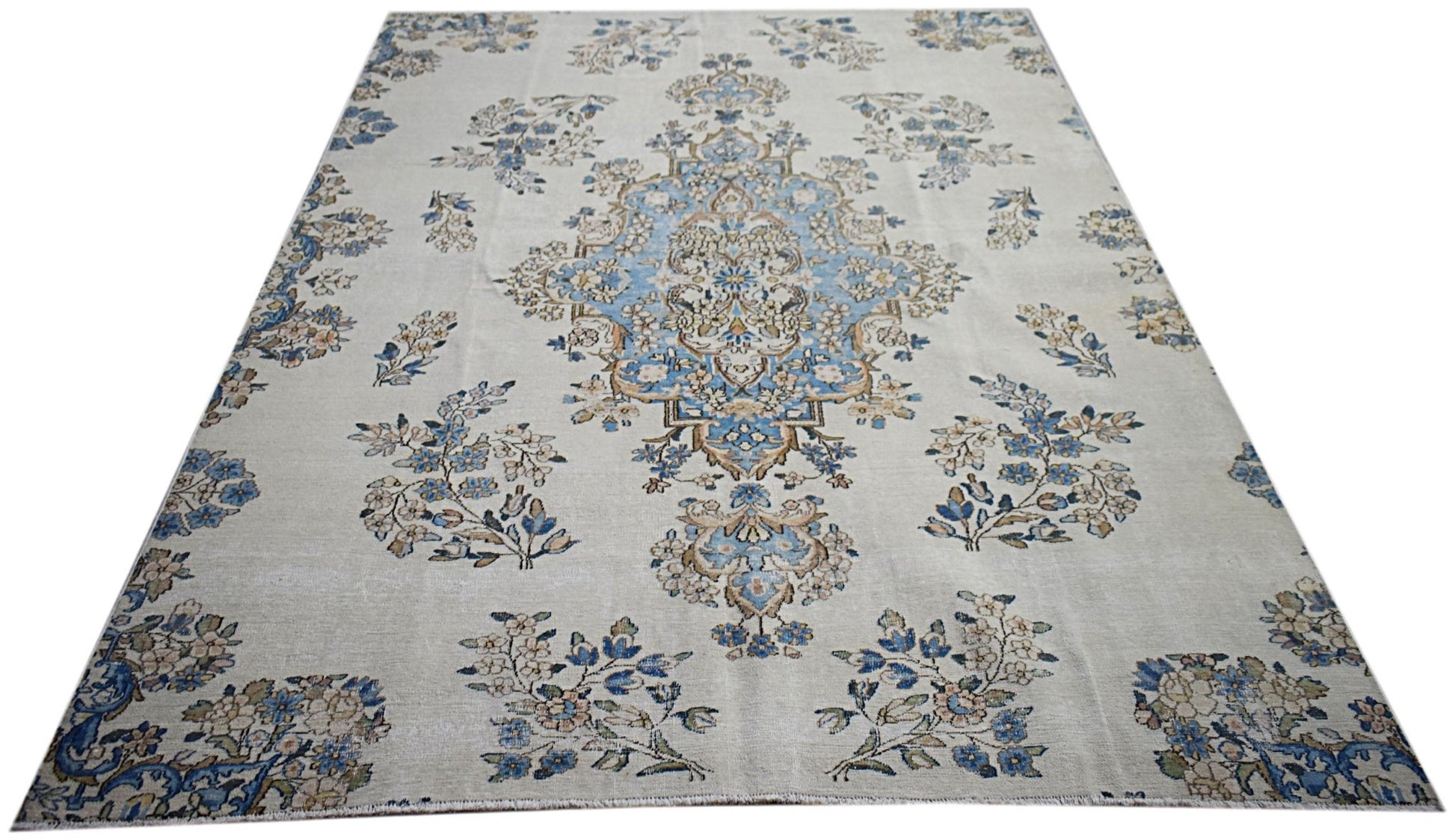 A vintage Persian Kerman rug featuring a central blue medallion and intricate floral motifs.