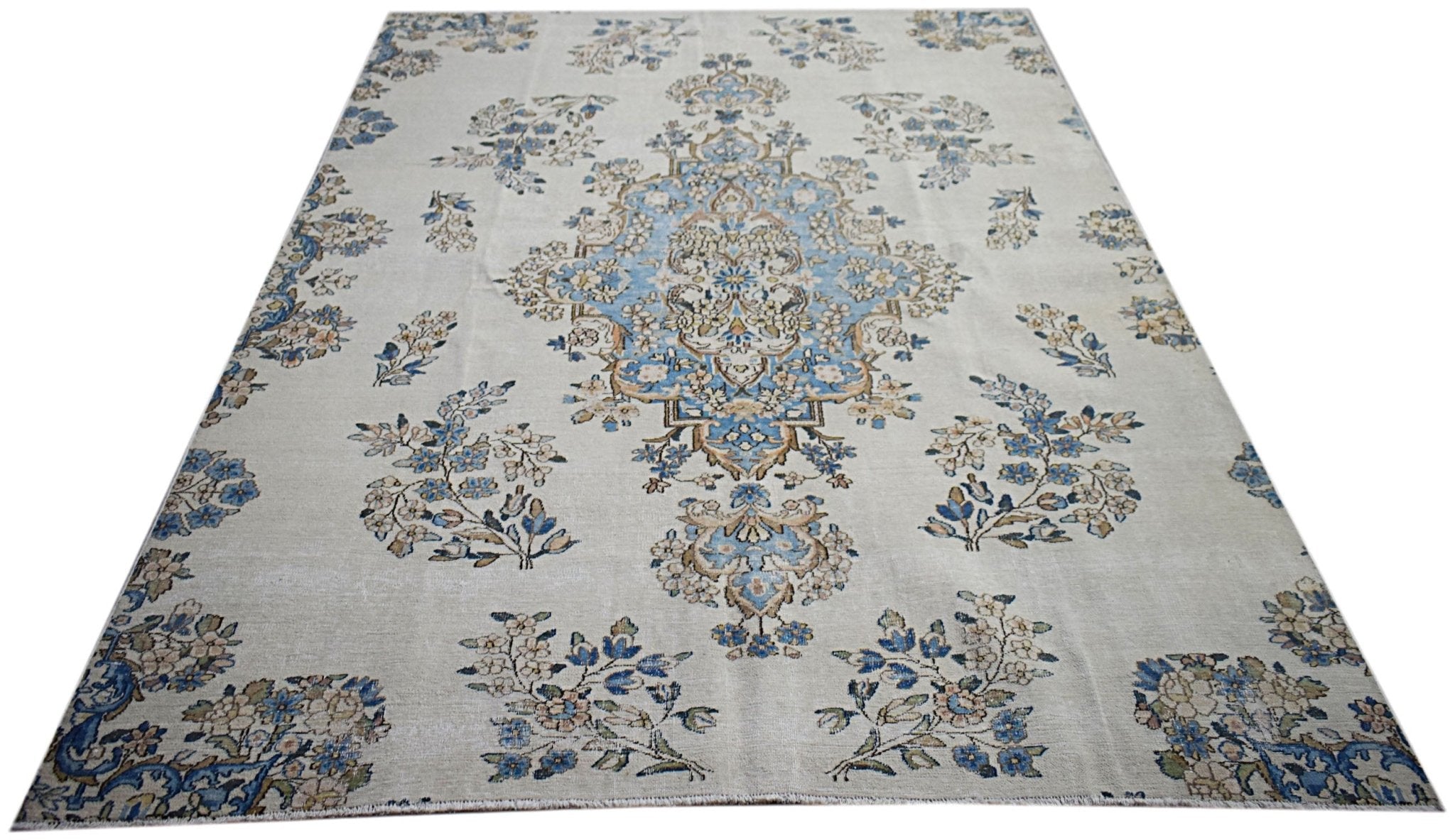 A vintage Persian Kerman rug featuring a central blue medallion and intricate floral motifs.