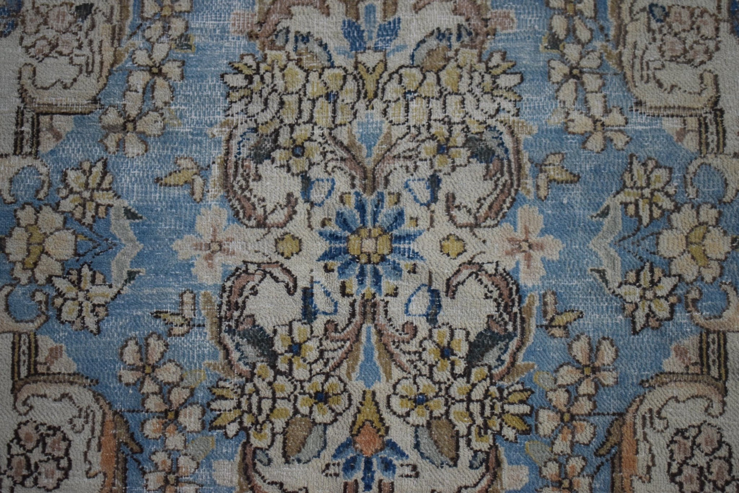 A vintage Persian Kerman rug featuring an intricate floral medallion pattern in blue and cream.