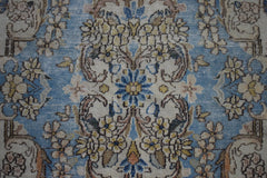 A vintage Persian Kerman rug featuring an intricate floral medallion pattern in blue and cream.