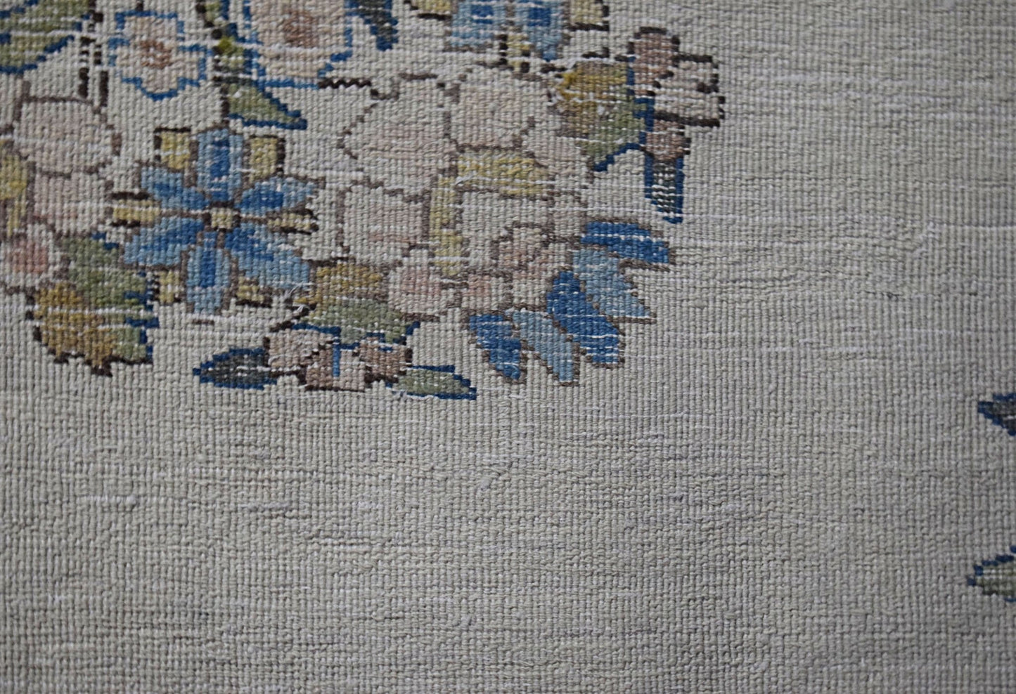 A close-up of a vintage Persian Kerman rug featuring intricate floral patterns on a cream field.