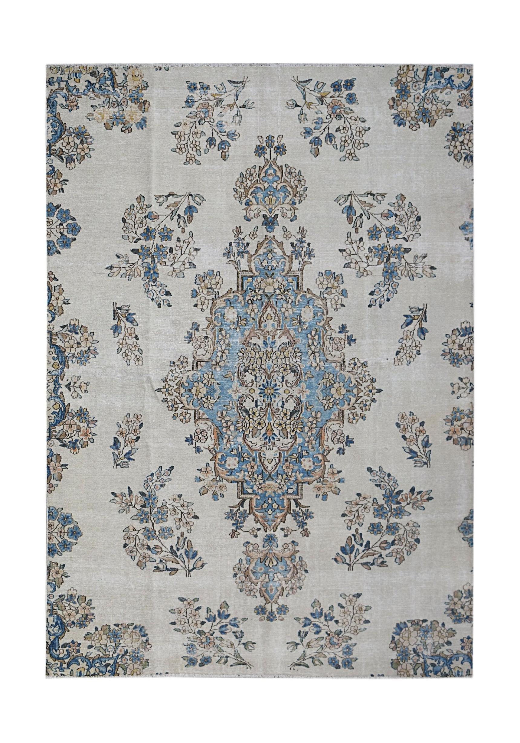 A vintage Persian Kerman rug featuring a central blue floral medallion on a light cream field.