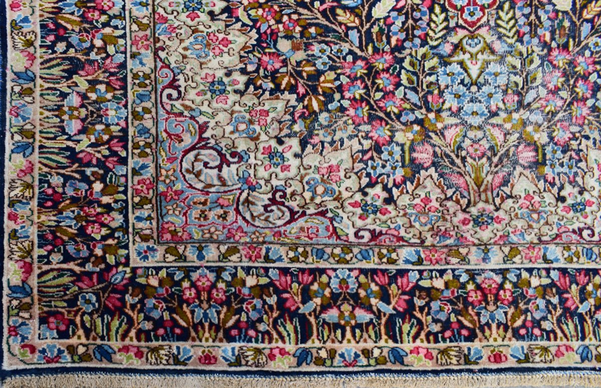A vintage Persian Kerman rug featuring an intricate floral pattern in blue, pink, and cream tones.