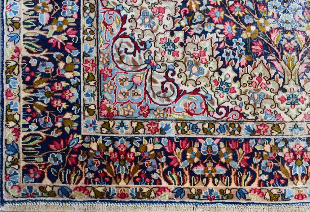 A vintage Persian Kerman rug featuring an intricate floral pattern in blue, pink, and cream tones.