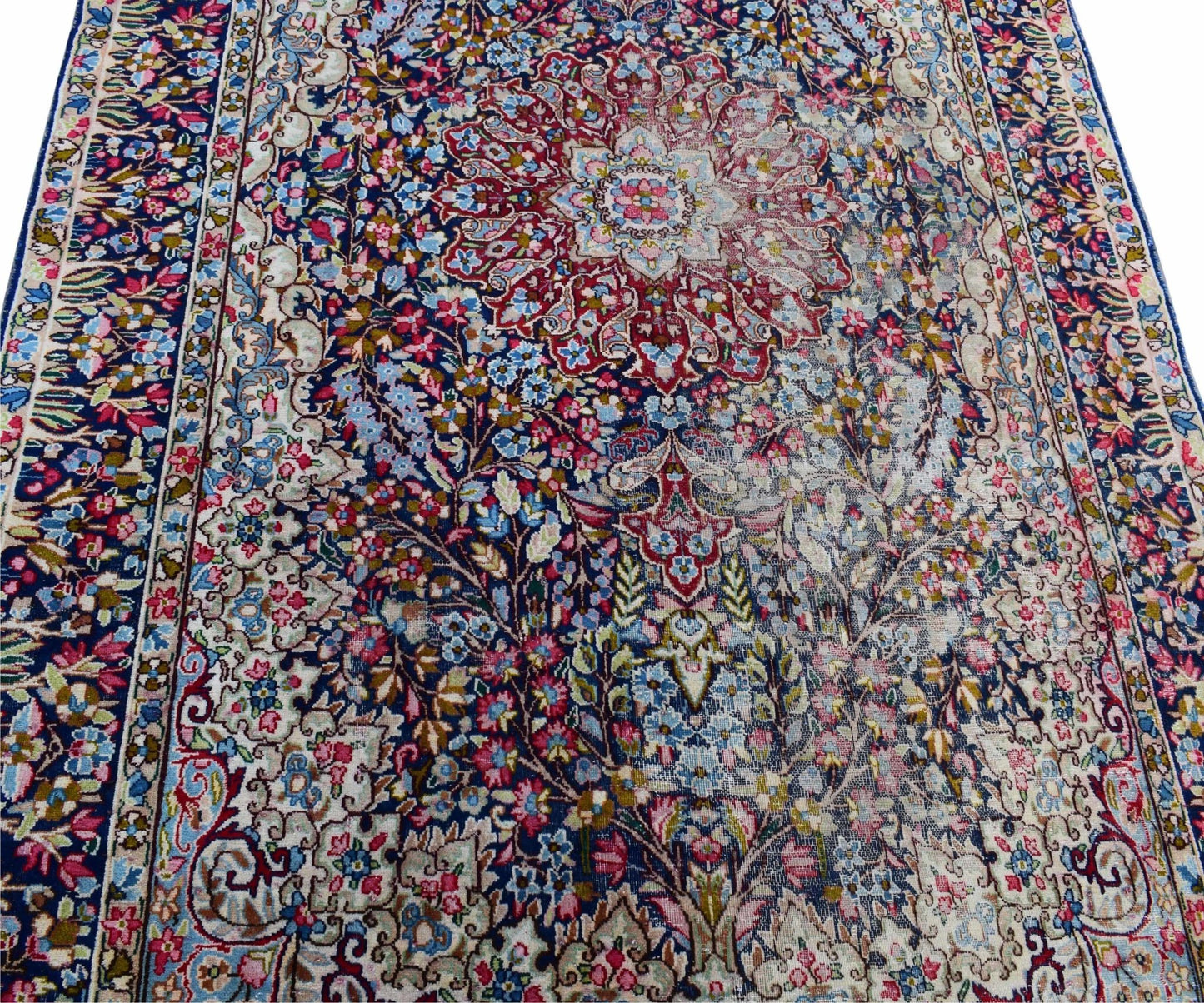 A vintage Persian Kerman rug featuring an intricate floral medallion design on a dark blue field.