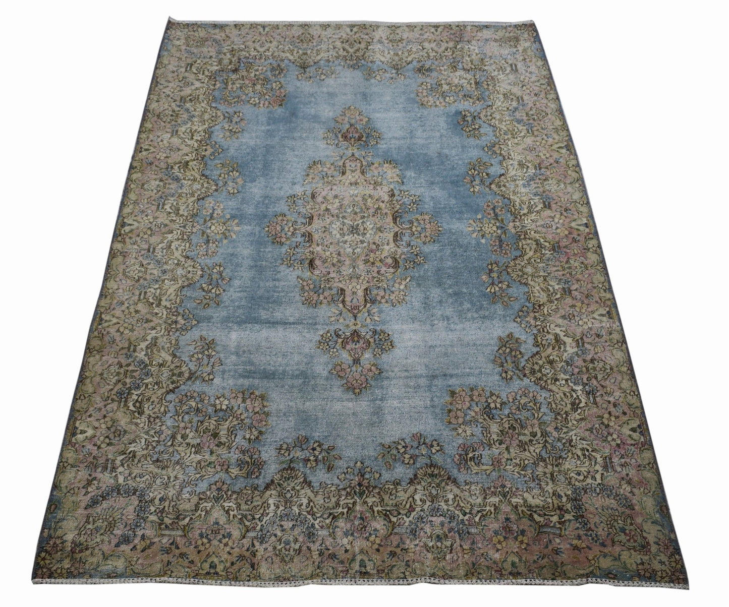 A vintage Persian Kerman rug featuring a central floral medallion on a faded blue field.