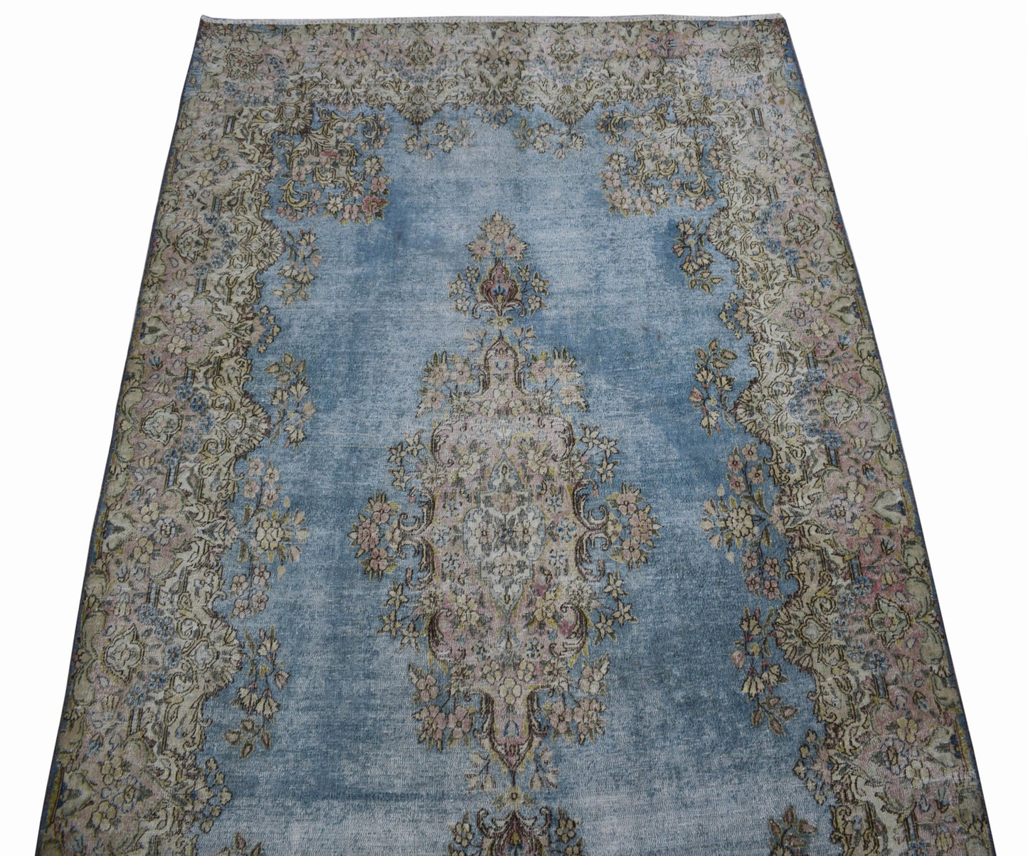 A vintage Persian Kerman rug featuring a central floral medallion on a faded blue field.
