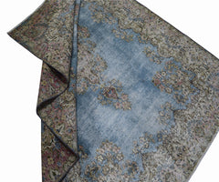 A vintage Persian Kerman rug featuring a faded blue field with intricate floral patterns.