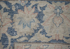 A close-up of a vintage Persian Kerman rug featuring intricate floral patterns in blue and tan.