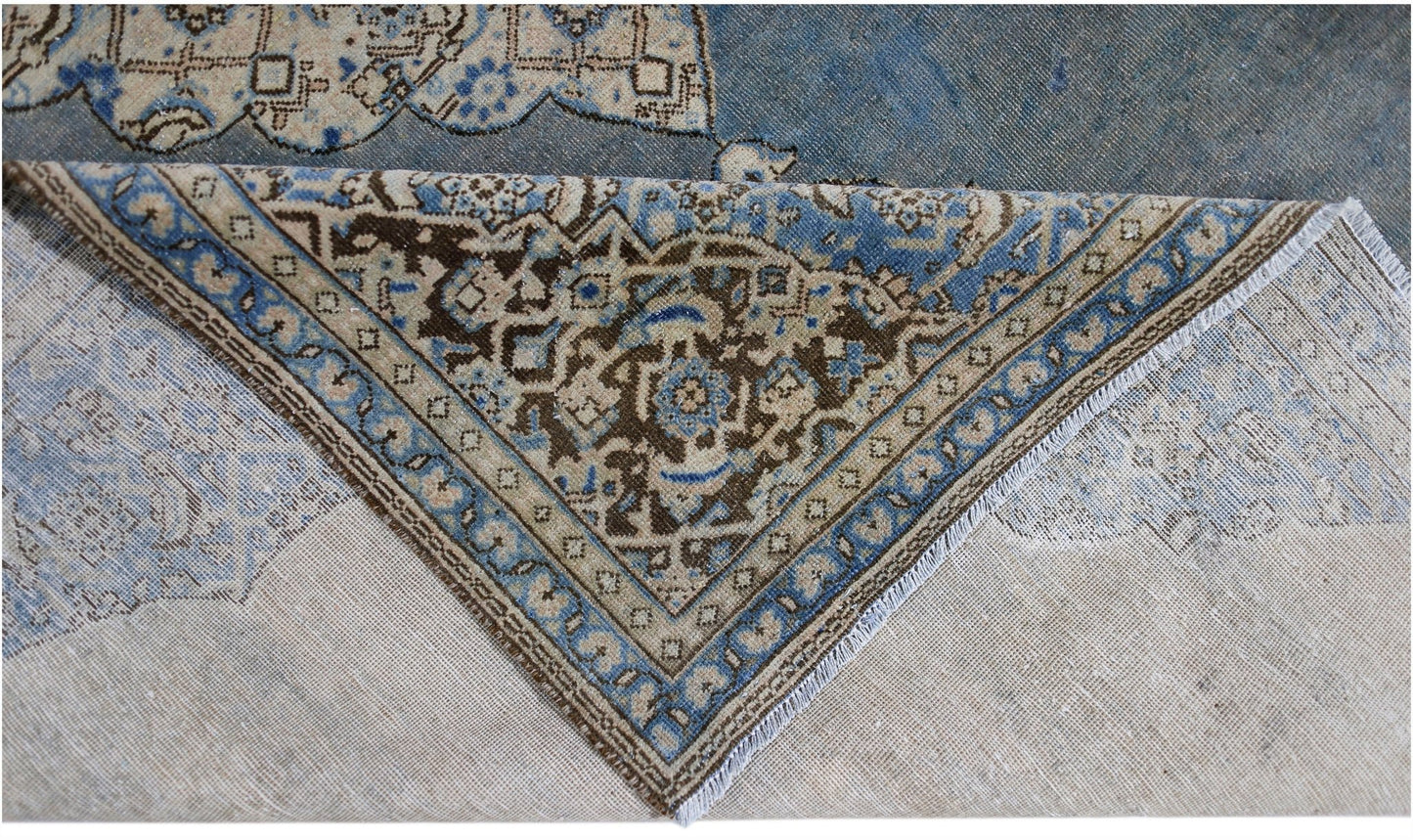 A corner of a vintage Persian Kerman rug is folded back to reveal its intricate floral pattern.