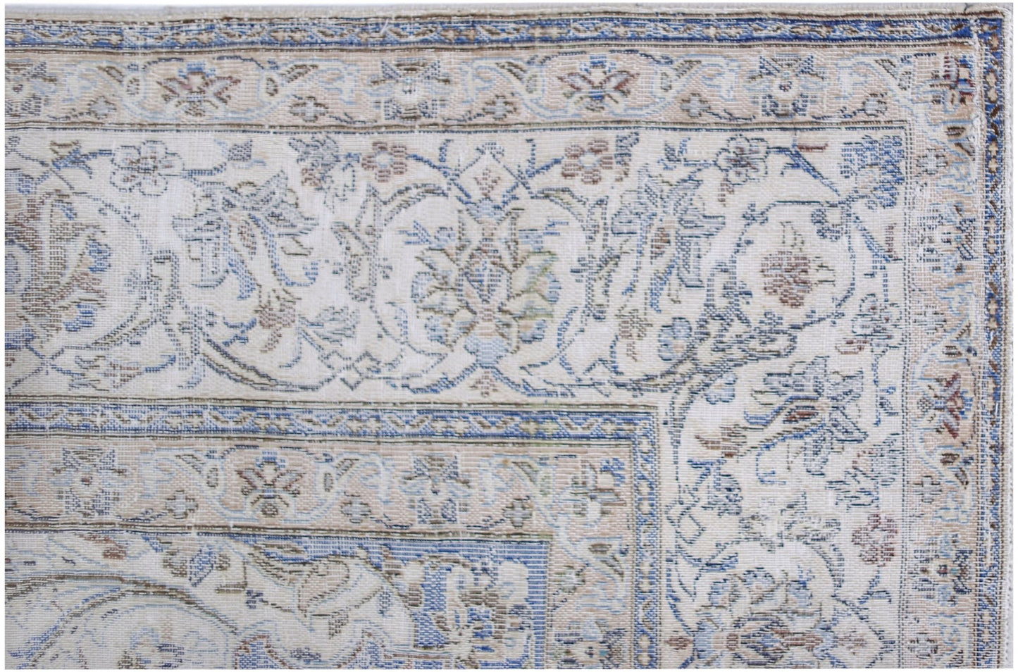 A close-up of a vintage Persian Kerman rug featuring intricate floral patterns in blue and beige.