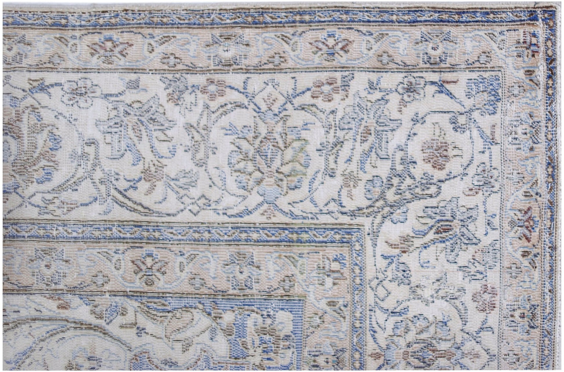 A close-up of a vintage Persian Kerman rug featuring intricate floral patterns in blue and beige.