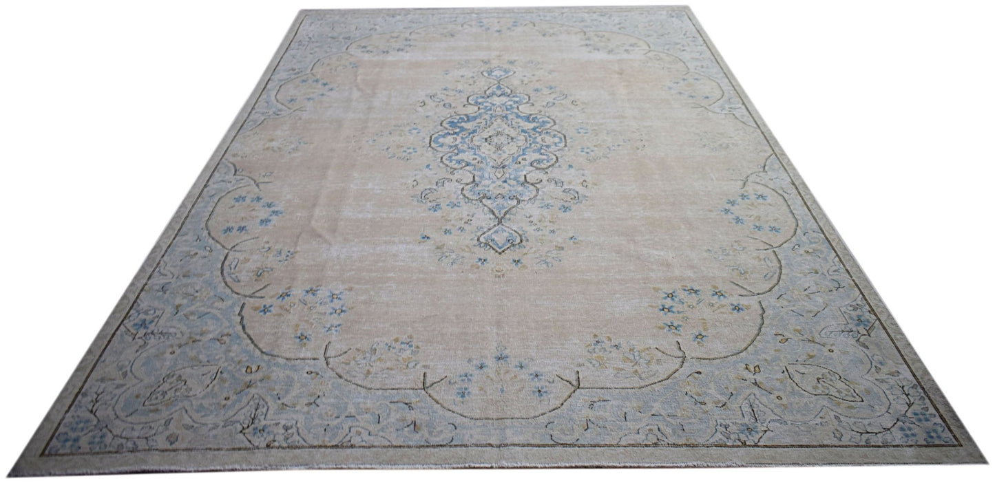 A vintage Persian Kerman rug featuring a central blue medallion on a soft beige floral field.