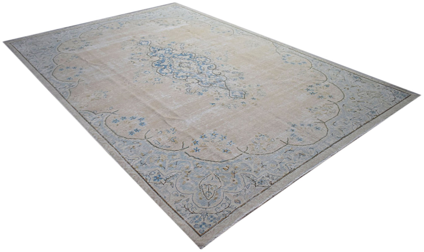 A vintage Persian Kerman rug featuring a central blue medallion on a beige floral field.