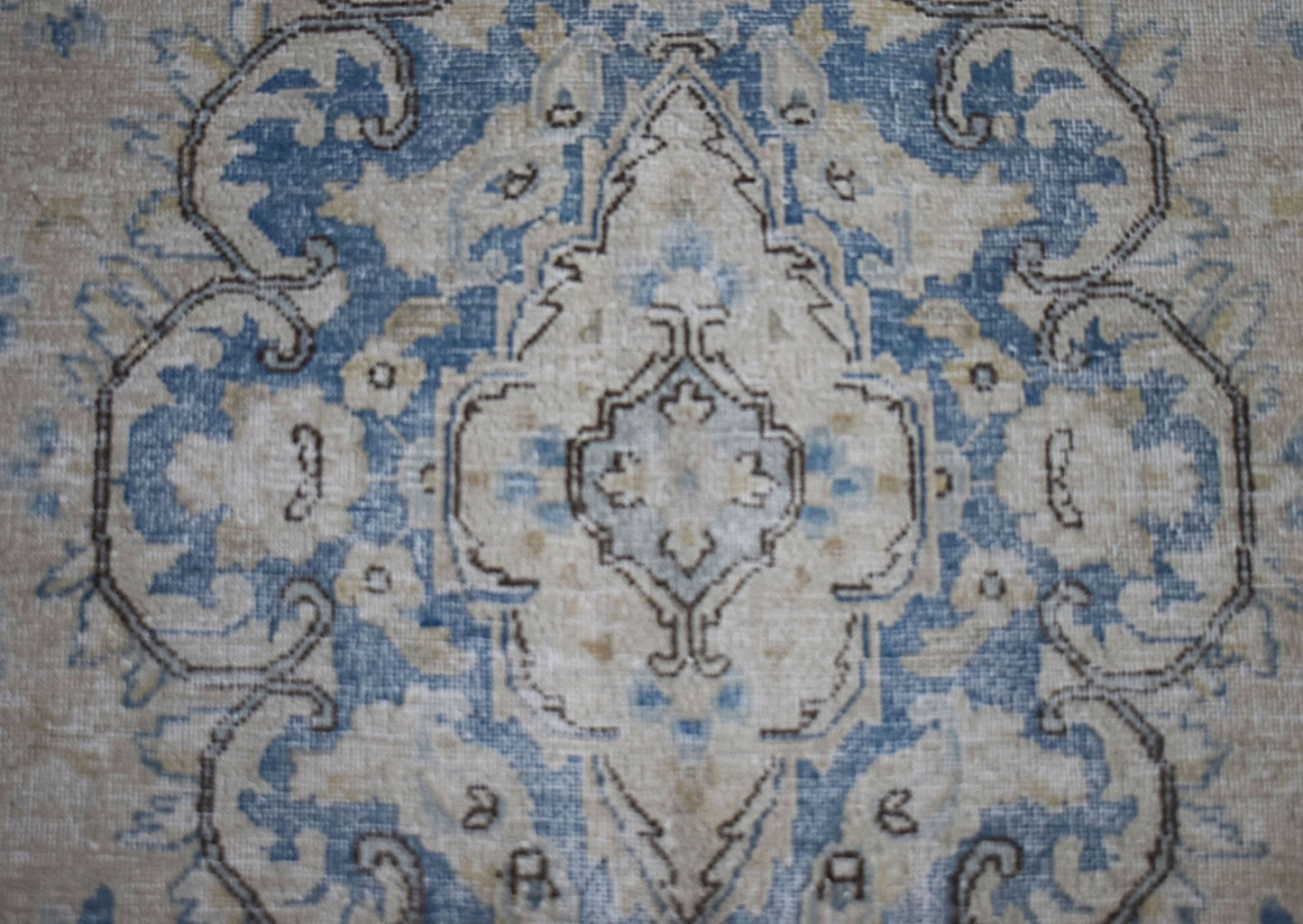 A vintage Persian Kerman rug featuring a central medallion with intricate blue and beige floral motifs.