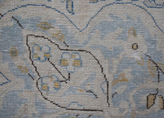A close-up of a vintage Persian Kerman rug featuring intricate floral patterns in soft blue tones.